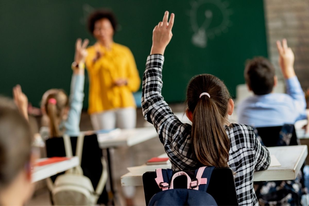 Rear view of schoolgirl raising her arm to answer the question in the classroom