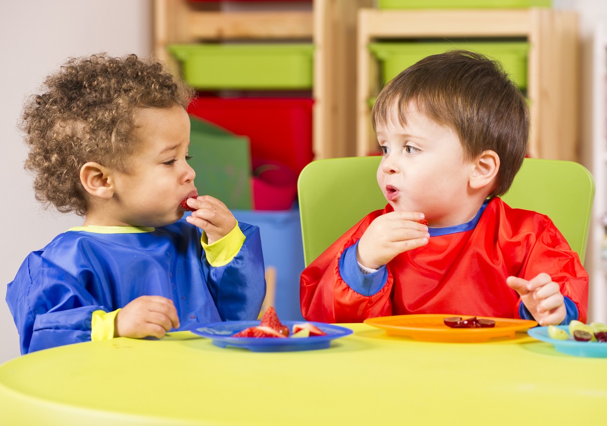 Two toddlers eating fruit in a nursery