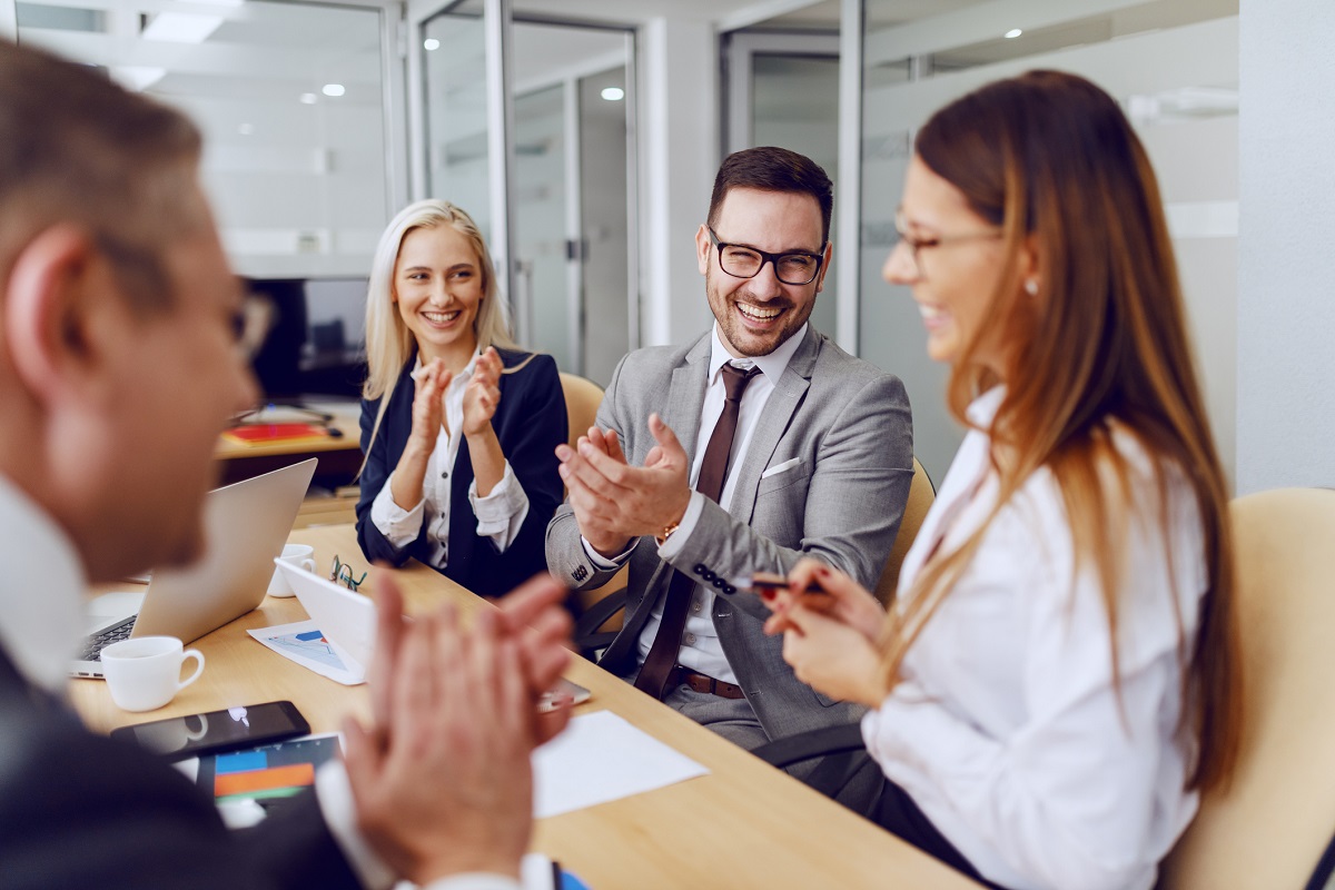 Colleagues clapping to their female colleague in boardroom