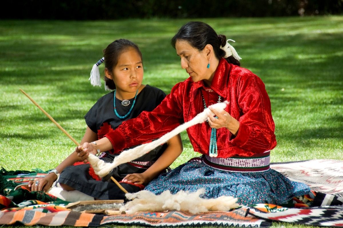 Native American woman teaches weaving to a young girl