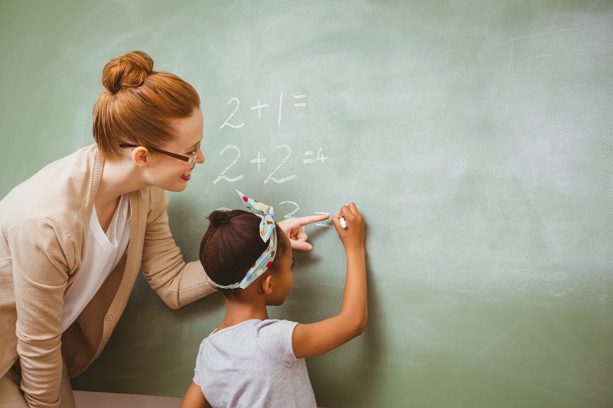 Teacher helps female student with math at blackboard