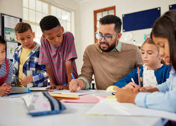 Teacher seated at a table speaking to young students