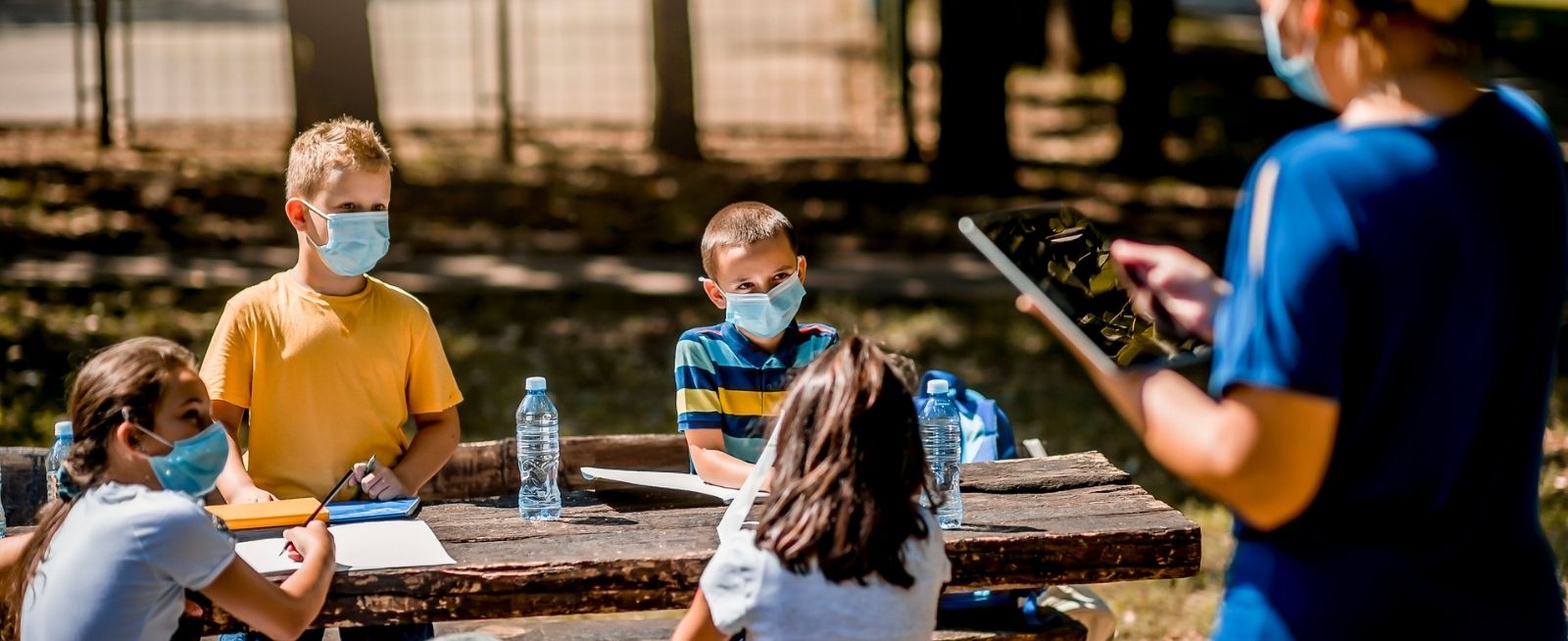 Group of school children with masks enjoying a class with their teacher outdoors