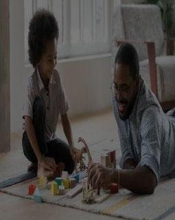 Young father and young son play with wooden block toys on living room floor