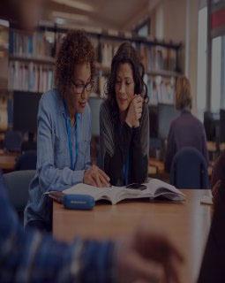 Teacher with mature female adult student sitting at table working in college library