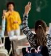 Rear view of schoolgirl raising her arm to answer the question in the classroom