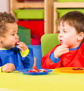 Two toddlers eating fruit in a nursery